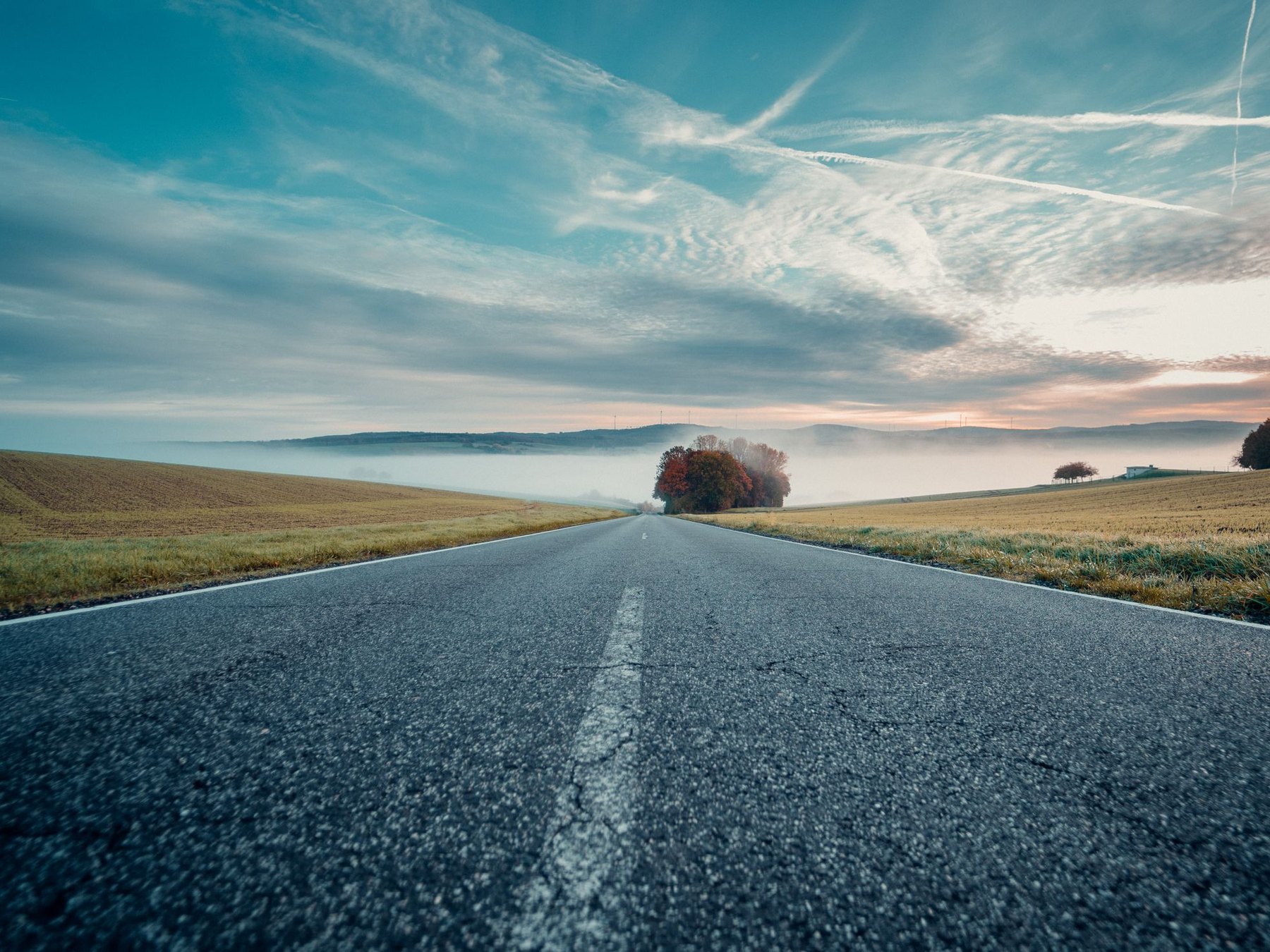 An empty two-lane road running straight toward a bright horizon at first light