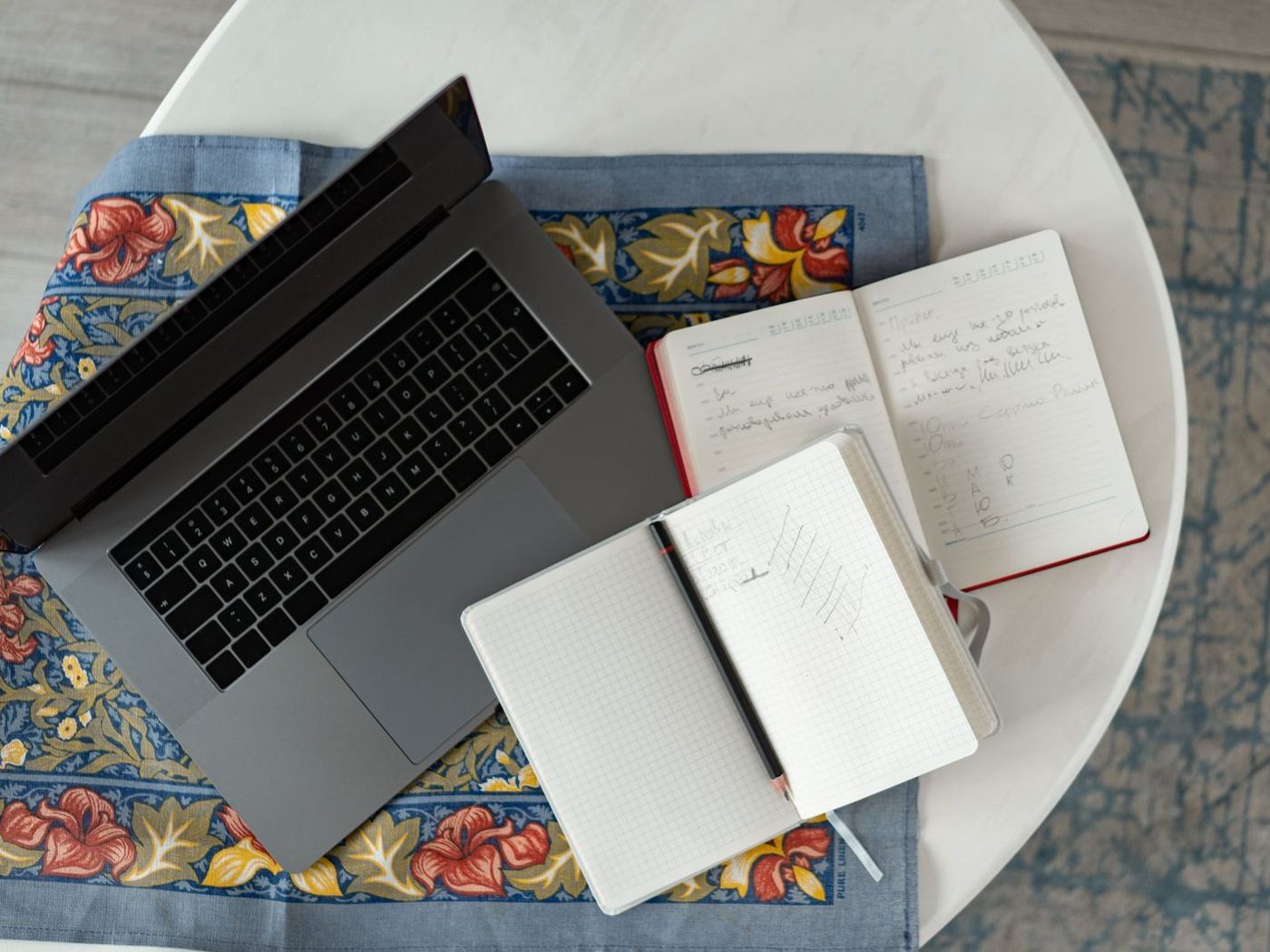 An open laptop beside two handwritten notebooks on a table, a plan being worked out on paper